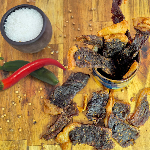 Biltong with chili and a pot of salt on a wooden chopping board