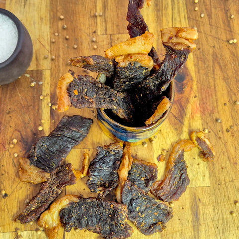 Biltong sliced sticks on a wooden board with a pot of salt