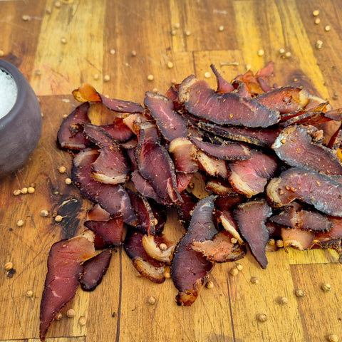 Traditional South African wet and fatty biltong on a wooden board with a pot of salt