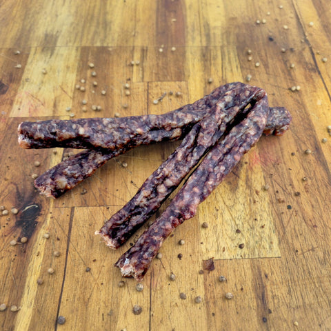 Four pieces of dried sausage or droewors on a wooden surface